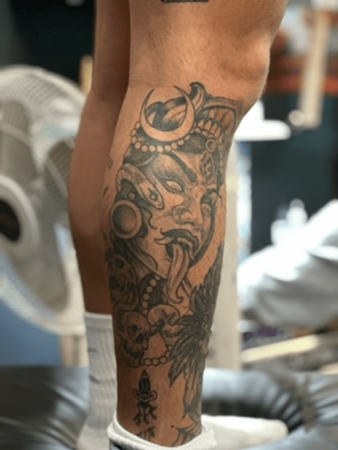 Blackwork tattoo of an ornate face and skulls on calf.